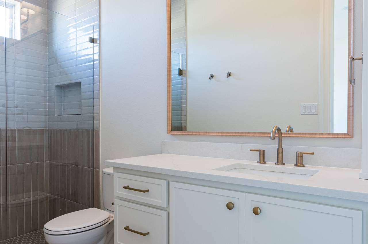 Another secondary bathroom with painted cabinets and earth tone tile floors and shower.