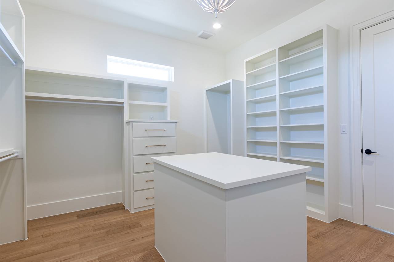 Primary walk-in closet features lots of built-in cabinets and wood flooring.