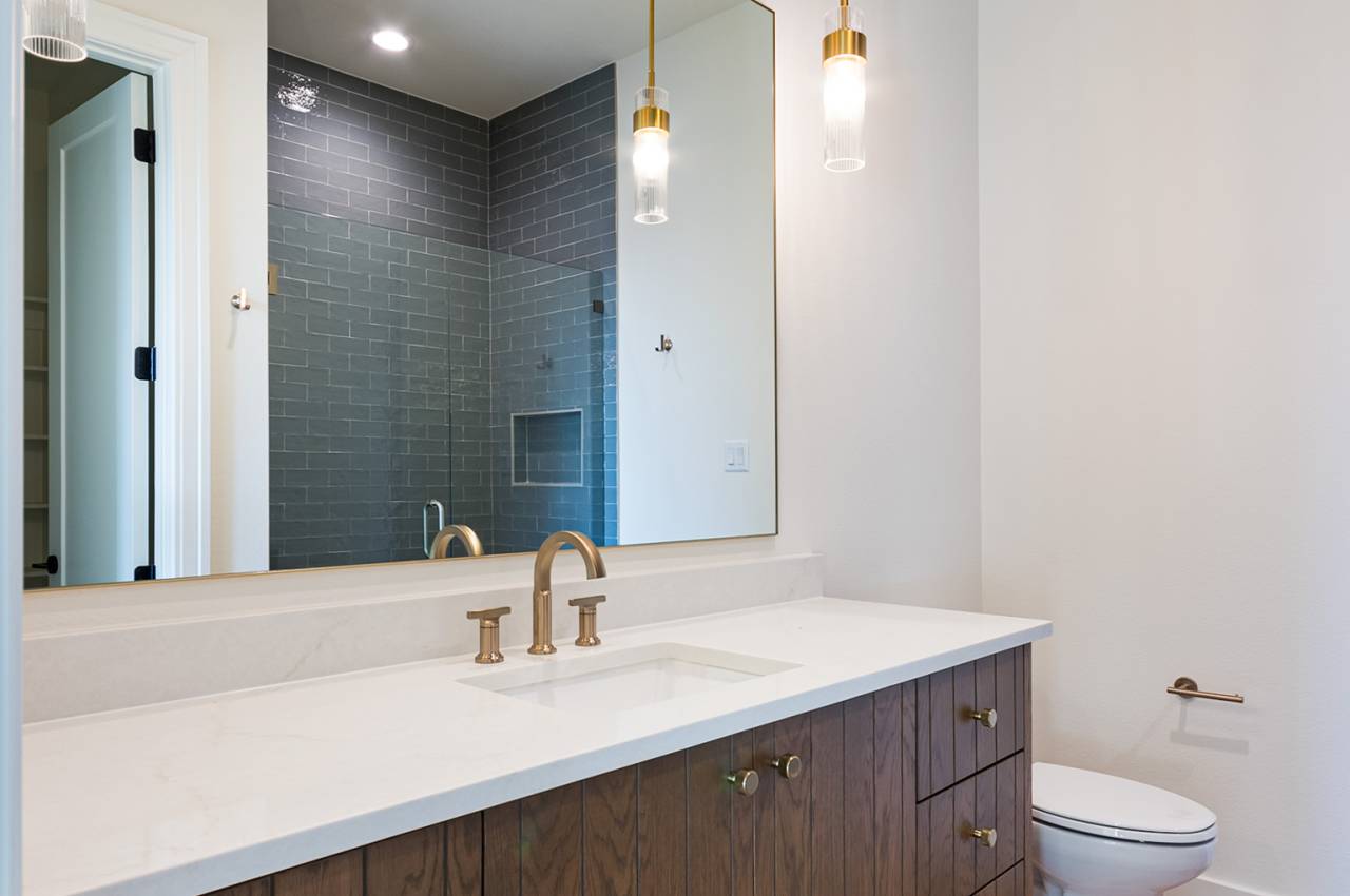 One of the secondary bathrooms features clean-lined, stained cabinets with earth tone floor tiles and decorator lighting.