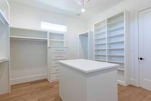 Primary walk-in closet features lots of built-in cabinets and wood flooring.